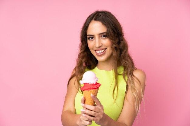 Young woman holding a cornet ice cream over on a pink wall