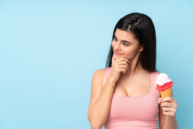 Giovane donna che tiene un gelato della cornetta che pensa un'idea e che guarda lato