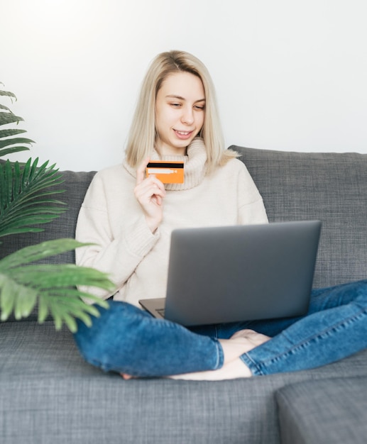 写真 クレジットカードを握ってラップトップコンピュータを使っている若い女性 オンラインショッピング インターネットバンキング 自宅から働く少女