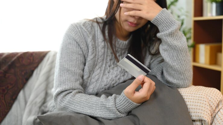 クレジットカードを持ち顔を覆ってストレスや心配を感じている若い女性