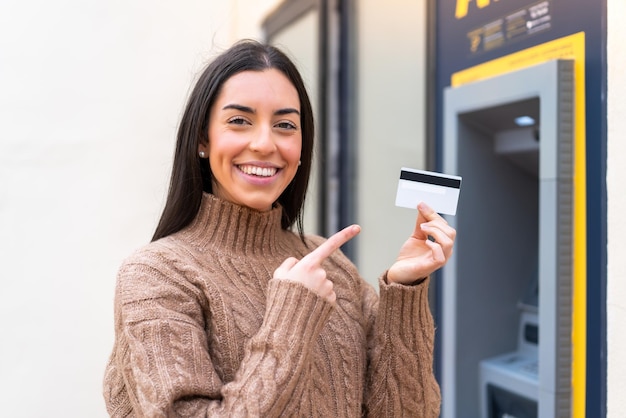 Молодая женщина держит кредитную карту на улице и указывает на нее