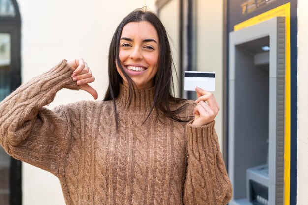 Young woman holding a credit card at outdoors proud and selfsatisfied