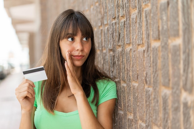 야외에서 뭔가 속삭이는 신용카드를 들고 있는 젊은 여성