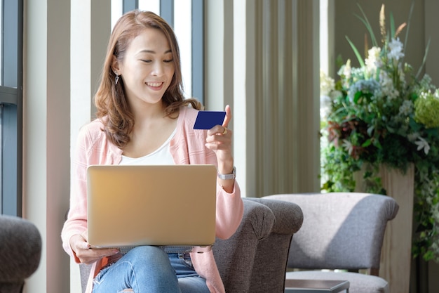 Young woman holding credit card for shopping online while using laptops in smiling mood.