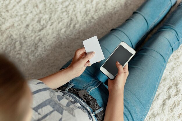 Young woman holding credit card and using phone sitting on floor Payment Online shopping concept