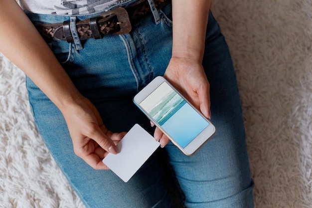 Young woman holding credit card and using phone sitting on floor Payment Online shopping