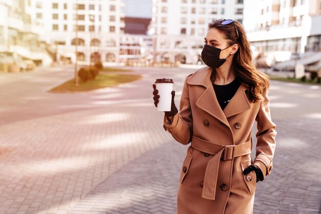 一杯のコーヒーを持ち、医療用保護マスクと手袋を着用している若い女性
