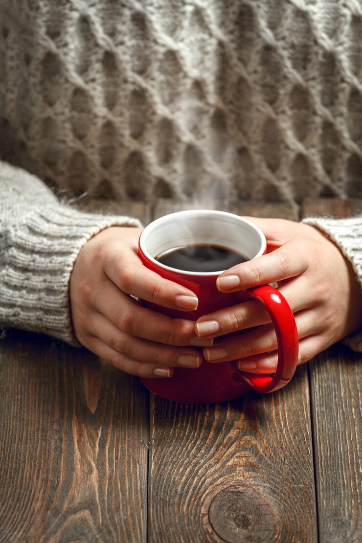 彼女の手でホットコーヒーのカップを保持している若い女性