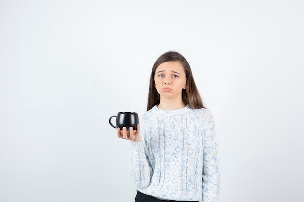 Young woman holding a cup of hot coffee over a white wall