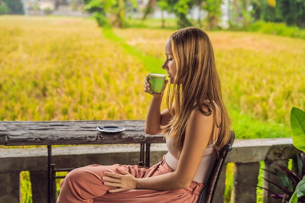 古い木製の背景のテーブルに抹茶ラテ、緑茶のカップを保持している若い女性。