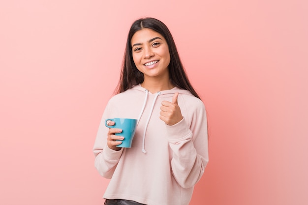 Young woman holding a cup smiling and raising thumb up