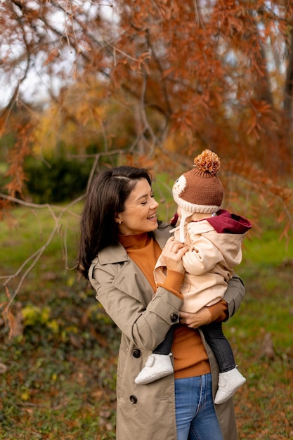 写真 秋の公園で可愛い赤ちゃんを抱いている若い女性