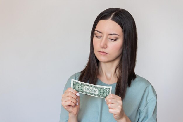 young woman holding a dollar bill in her hands looking at it and thinking where to spend the money