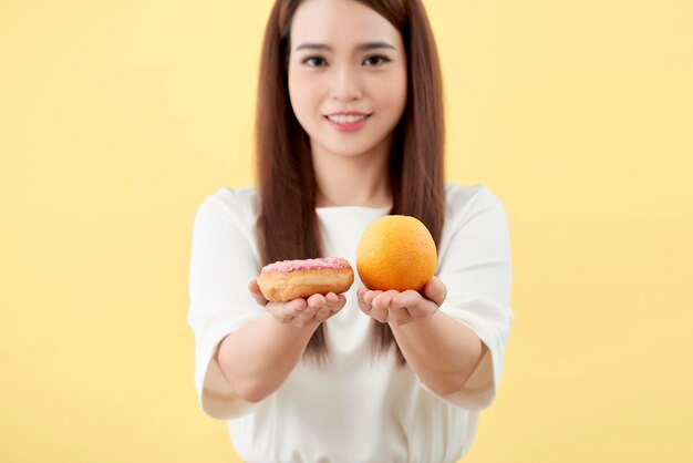 young woman holding donut and orange isolated on yellow background