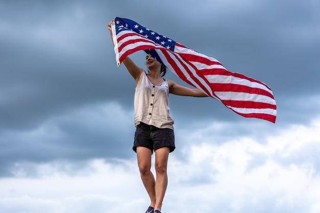 Young woman holding the flag of america against the background of the sky.