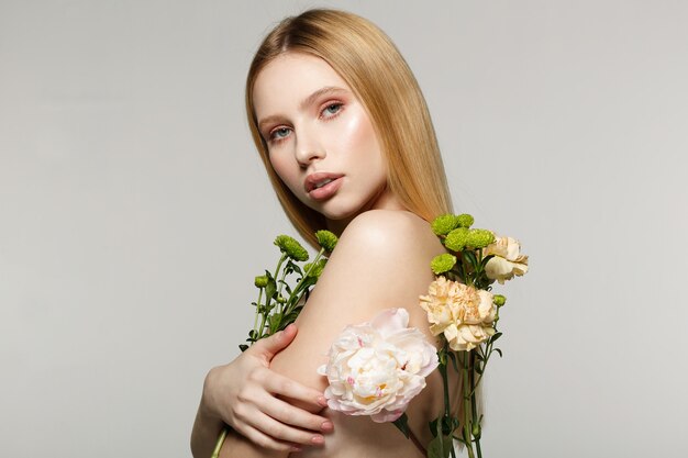 Young woman holding flowers and posing in a studio