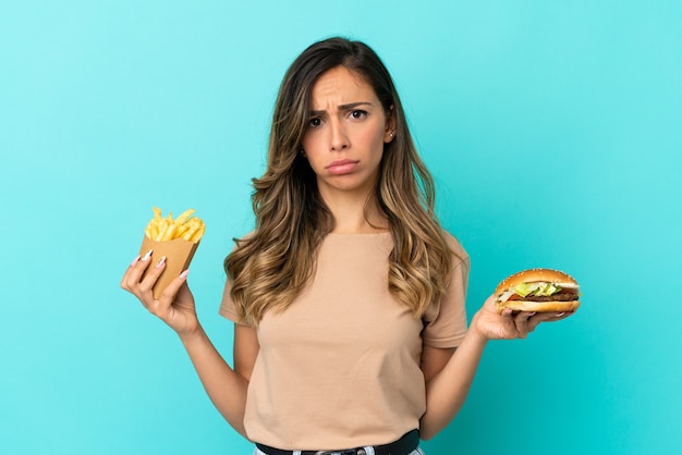 Фото Молодая женщина, держащая жареные чипсы и гамбургер на изолированном фоне
