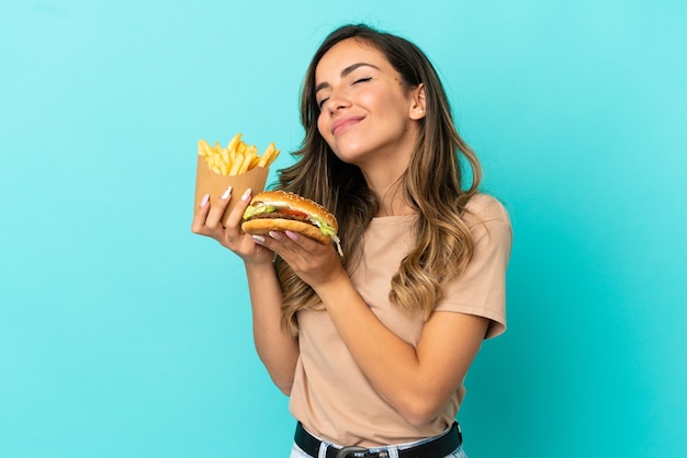 Young woman holding fried chips  and burger over isolated background