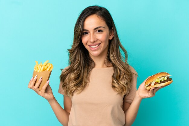 Young woman holding fried chips  and burger over isolated background