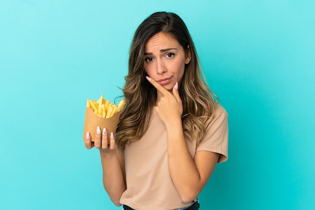 Young woman holding fried chips over isolated background thinking