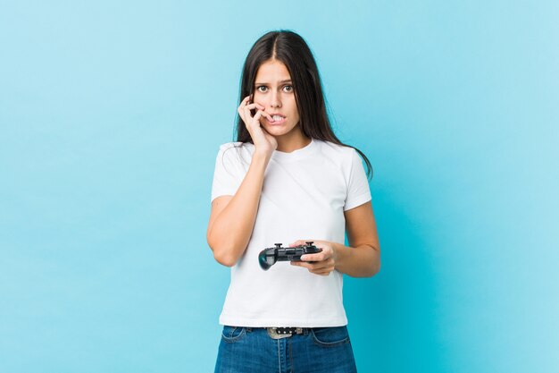 Young woman holding a game controller biting fingernails, nervous and very anxious