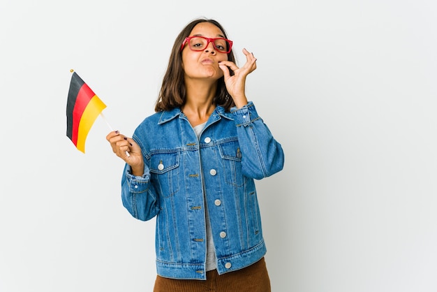 Young woman holding a german flag isolated on white wall with fingers on lips keeping a secret