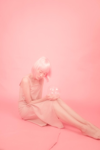 Young woman holding glass bowl while sitting over peach background