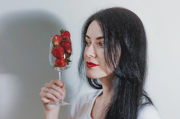 Young woman holding glass goblet of red strawberries in hand Concept of sexuality healthy eating