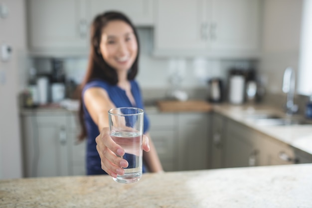 キッチンで水のガラスを保持している若い女性