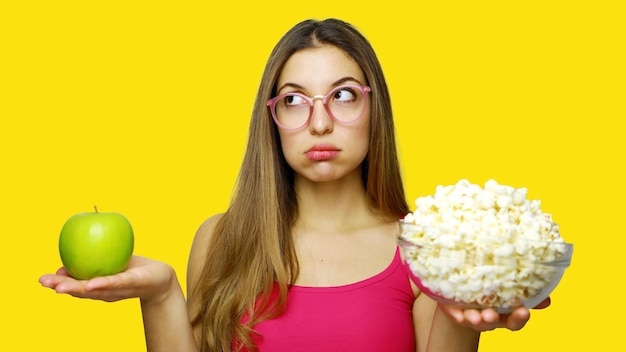 Foto giovane donna con in mano una mela di granny smith e una ciotola di popcorn sullo sfondo giallo