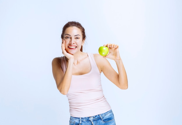Young woman holding a green apple and thinking