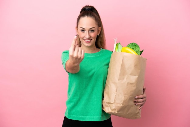 Young woman holding a grocery shopping bag doing coming gesture