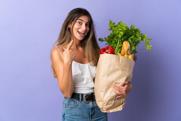 Young woman holding a grocery shopping bag giving a thumbs up gesture