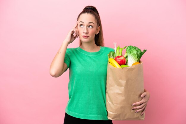 Young woman holding a grocery shopping bag having doubts and thinking