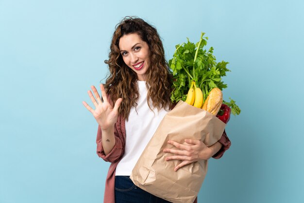 Young woman holding a grocery shopping bag isolated on blue counting five with fingers