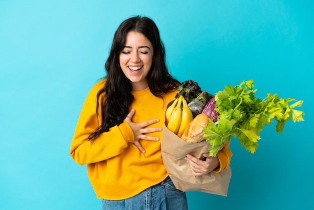 Young woman holding a grocery shopping bag isolated on blue smiling a lot