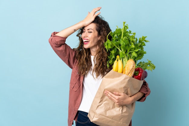 Young woman holding a grocery shopping bag isolated on blue wall has realized something and intending the solution