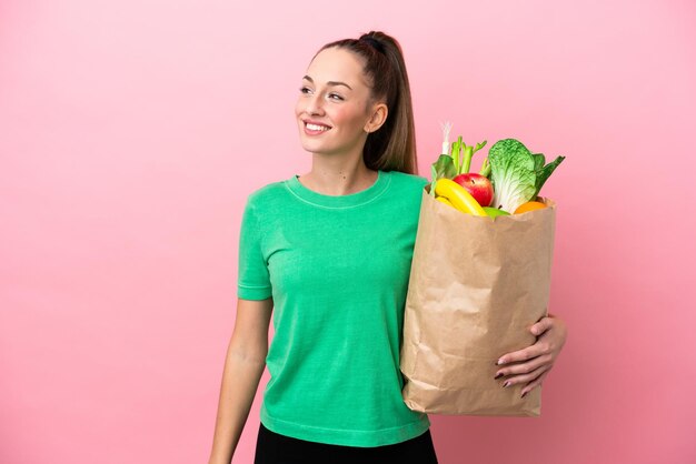 Young woman holding a grocery shopping bag looking to the side and smiling