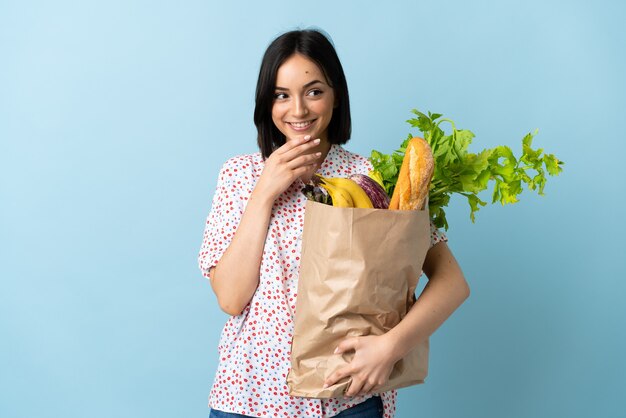 Young woman holding a grocery shopping bag looking up while smiling