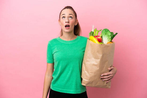 Young woman holding a grocery shopping bag looking up and with surprised expression