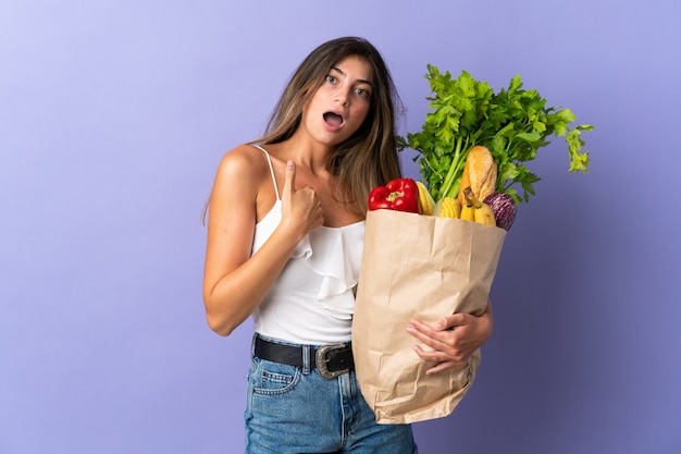 Young woman holding a grocery shopping bag with surprise facial expression
