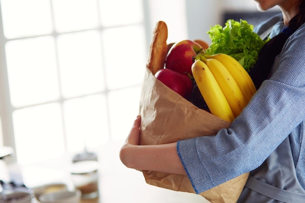 台所に立っている野菜と食料品の買い物袋を保持している若い女性