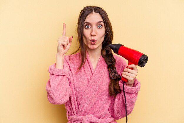 Young woman holding a hairdryer isolated on yellow background having some great idea concept of creativity