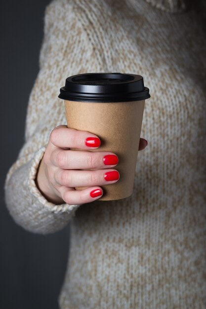 Young woman holding in hands blank take away kraft coffee cup, Light beige sweater.