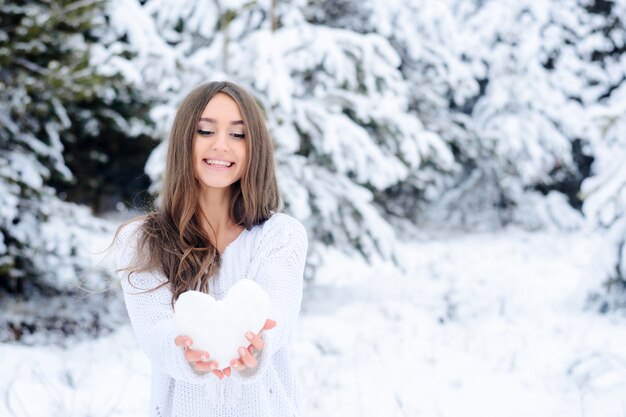 Young woman holding a heart from the snow in the winter forest.