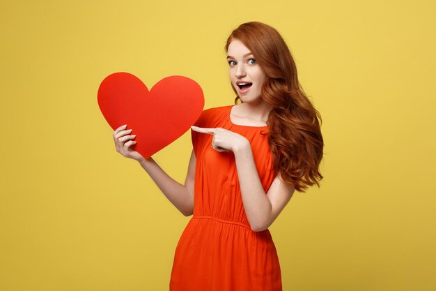 Young woman holding heart shape against orange background
