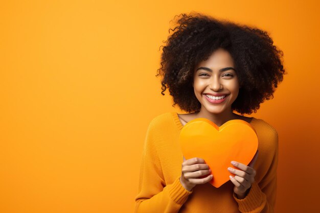 Young woman holding a heart shaped pillow against orange background