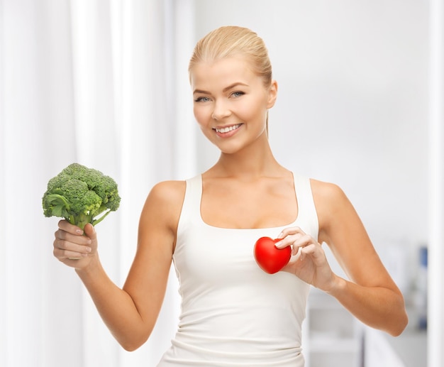 young woman holding heart symbol and broccoli