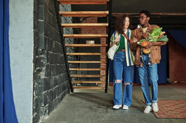 Young woman holding her boyfriend with fresh vegetables by his arm