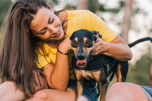 写真 草の上に座っている頭で彼女の犬を保持している若い女性。公園で彼女の犬と美しい女性